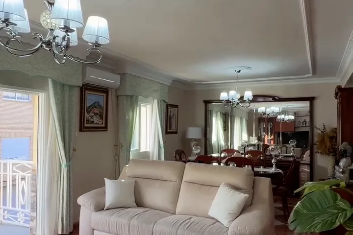 Salón de un piso con balcón a la calle, suelo de terrazo y lámpara de araña